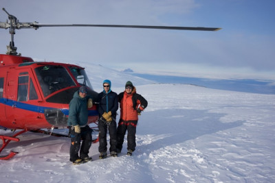 Hill, Uhlmann and Wannamaker stand beside a helicopter on snowy Mt Erebus